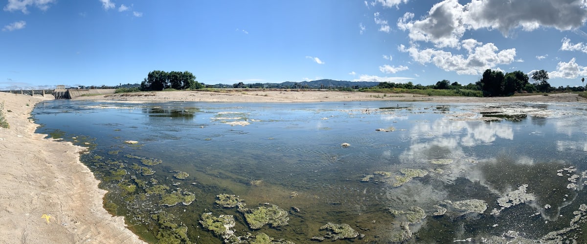 A river with clear water, sandy banks, and a bridge in the distance.