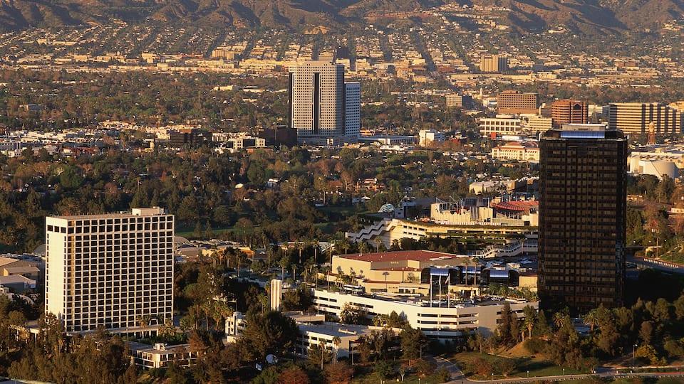 A cityscape with prominent buildings, including a large hotel and several high-rise structures, set against a backdrop of mountains and a dense urban area.