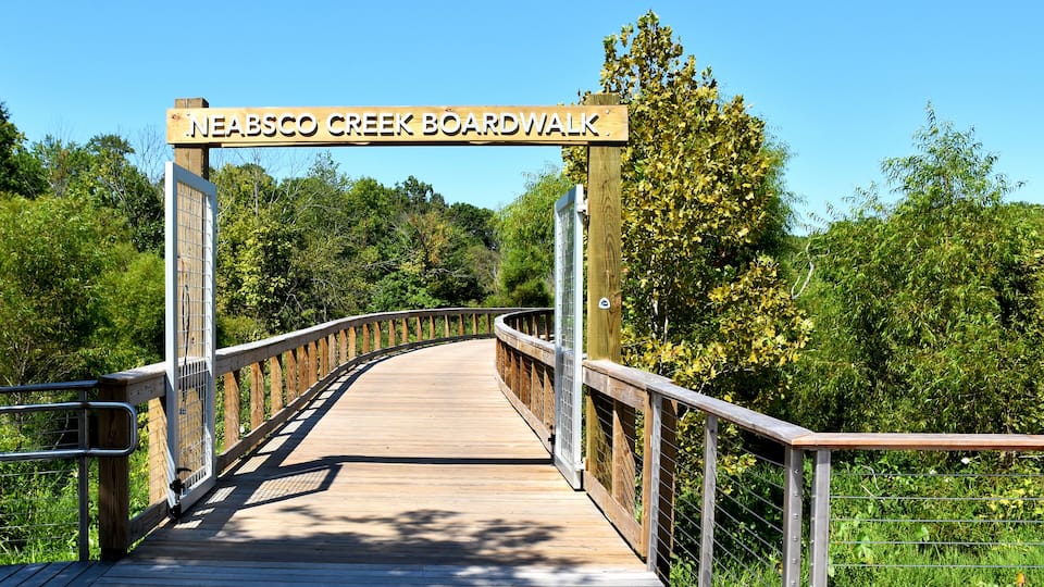 A wooden boardwalk at Neabscog Creek with metal railings and a sign overhead.