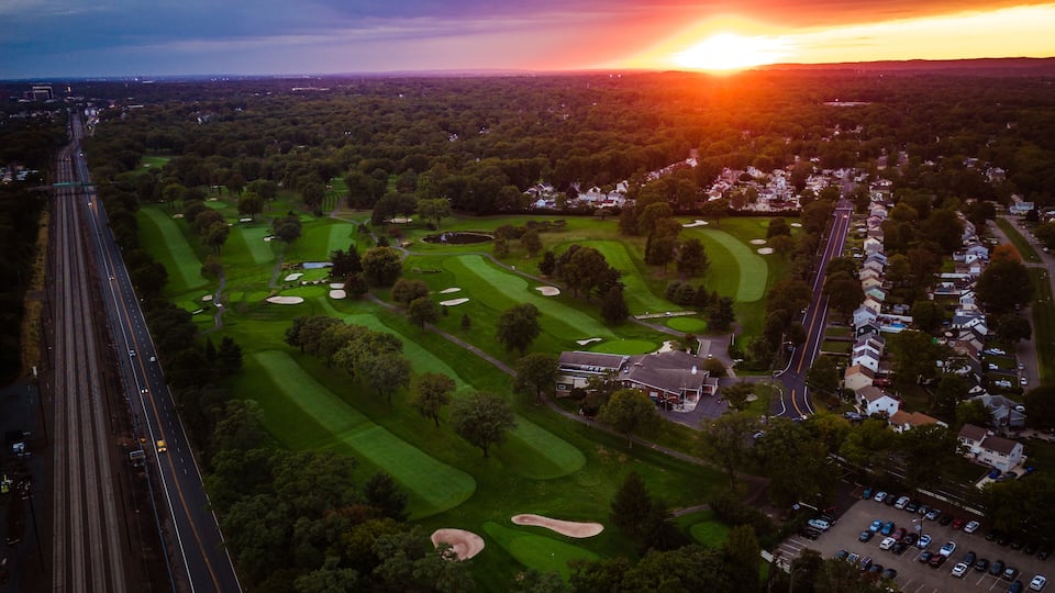 An aerial view of a golf course with a sunset in the background.