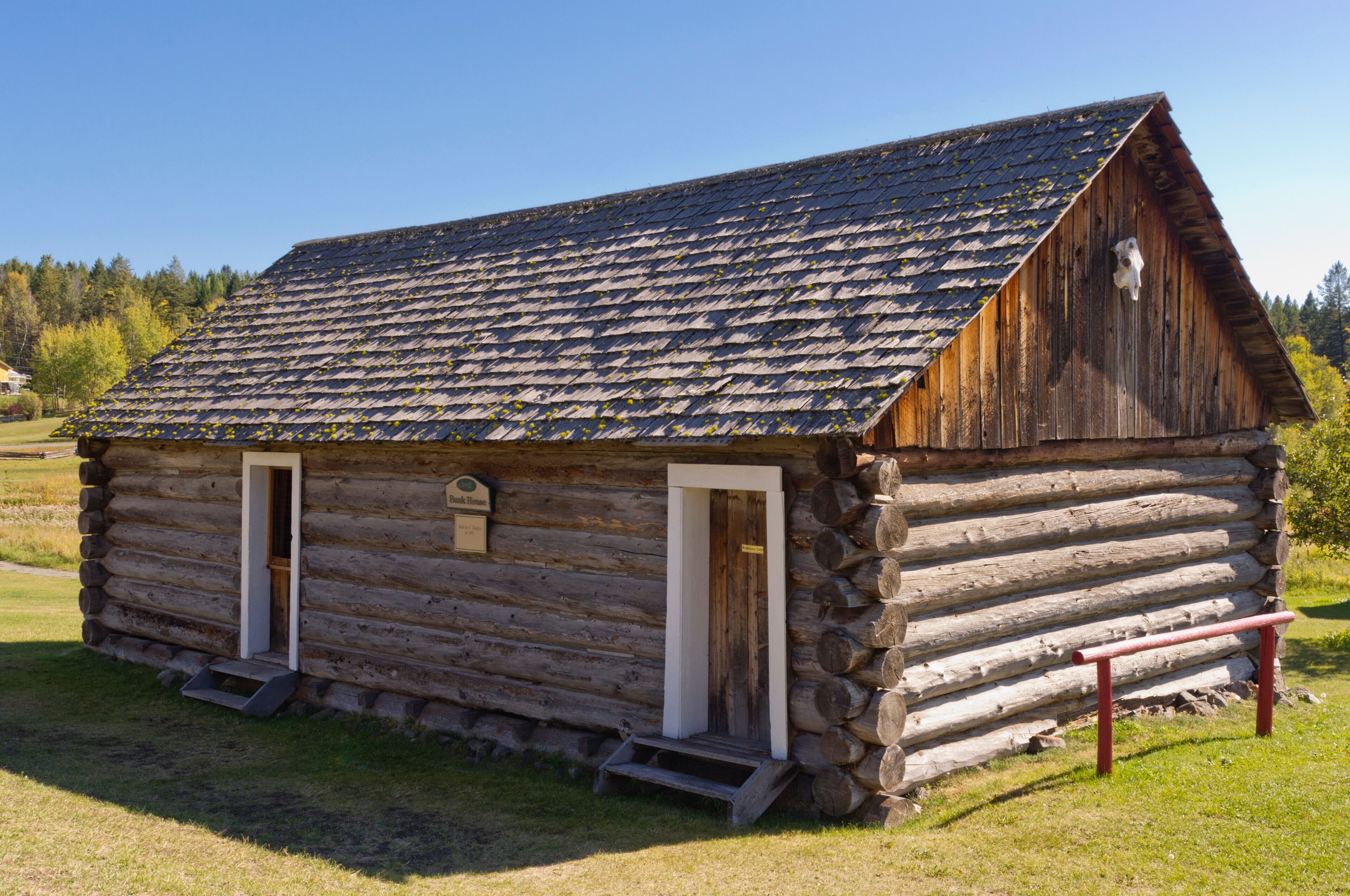 A rustic log cabin with a steeply pitched roof, two front doors, and a small porch.
