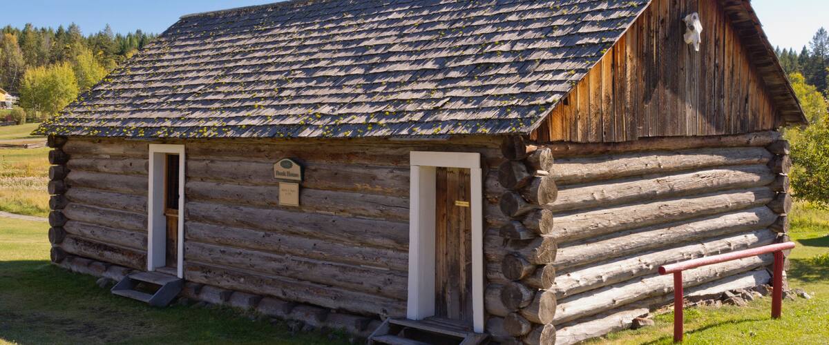A rustic log cabin with a steeply pitched roof, two front doors, and a small porch.