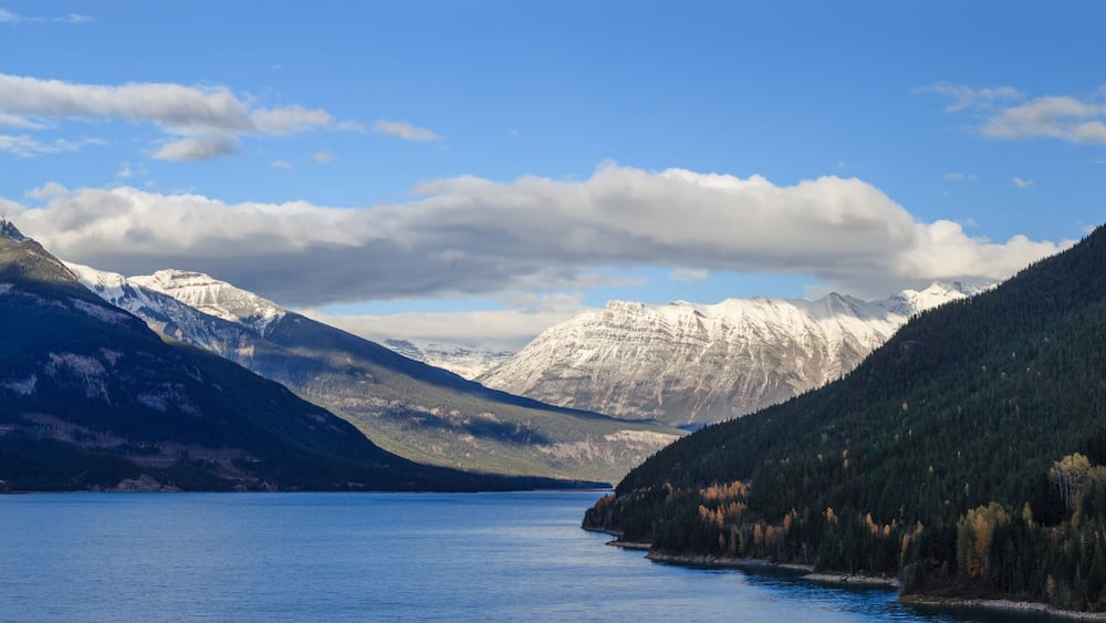 Ein See, umgeben von schneebedeckten Bergen und dichten Wäldern.