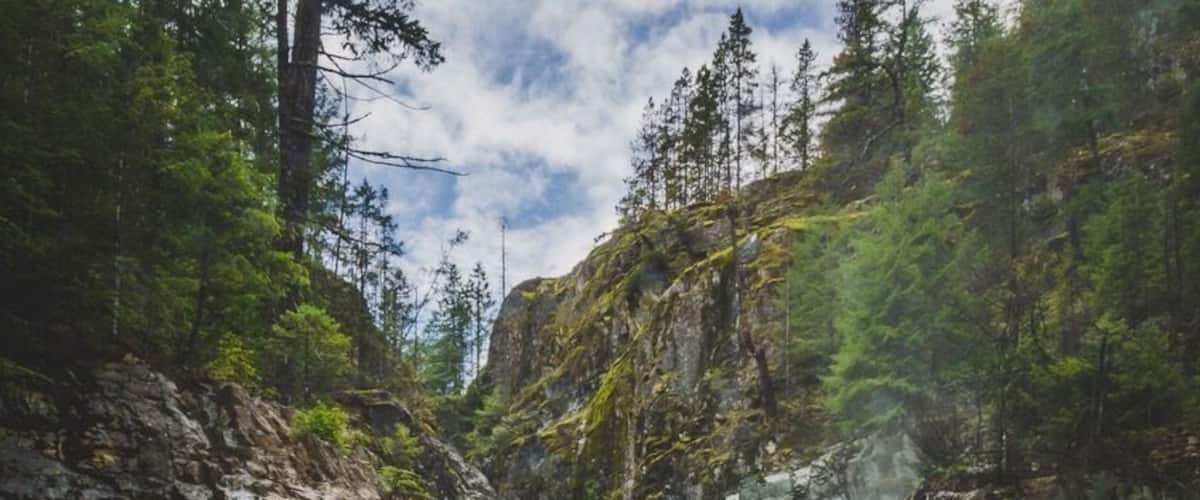 A waterfall cascading into a clear river surrounded by rocky cliffs and dense forest.