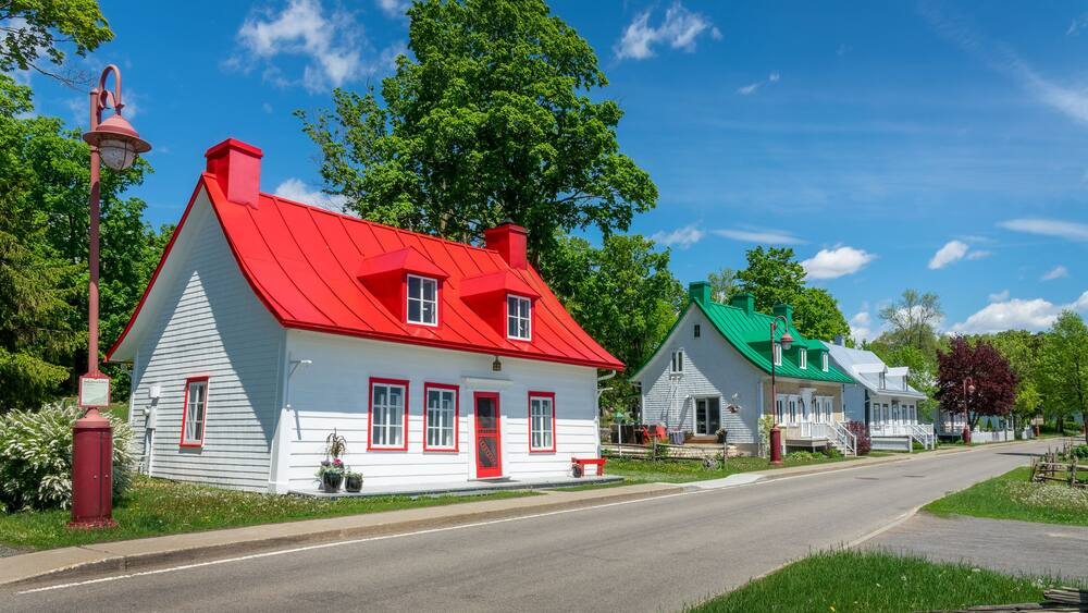 Une rangée de maisons pittoresques et colorées, avec des toits rouges et verts, un ciel bleu azur et de luxuriants arbres verdoyants.