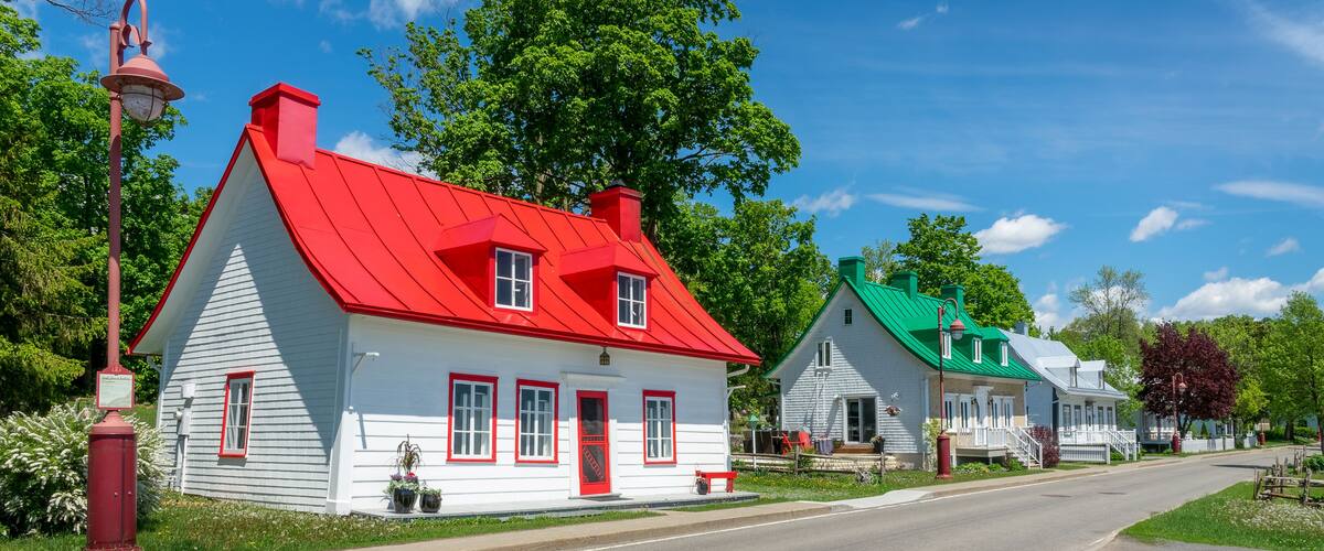 Eine Reihe von charmanten, farbenfrohen Häusern mit roten und grünen Dächern, einem klaren, blauen Himmel und üppigen, grünen Bäumen.