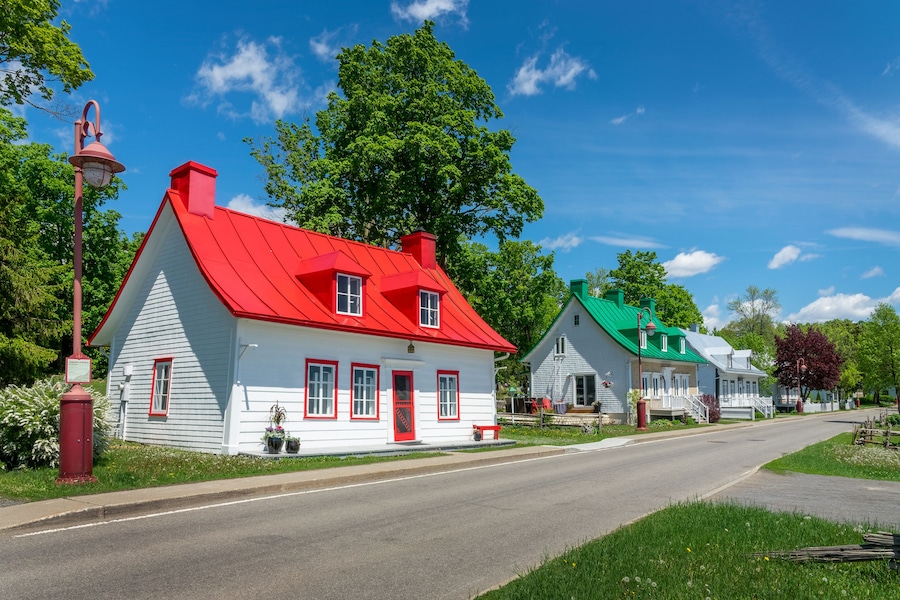 Una hilera de casas pintorescas y coloridas, con tejados rojos y verdes, un cielo azul despejado y árboles verdes y frondosos.