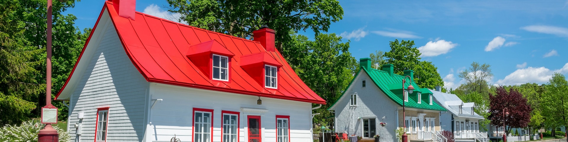 Una hilera de casas pintorescas y coloridas, con tejados rojos y verdes, un cielo azul despejado y árboles verdes y frondosos.