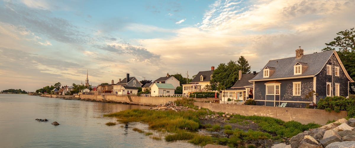 A waterfront village with houses along the shore, a church steeple in the distance, and a calm river.