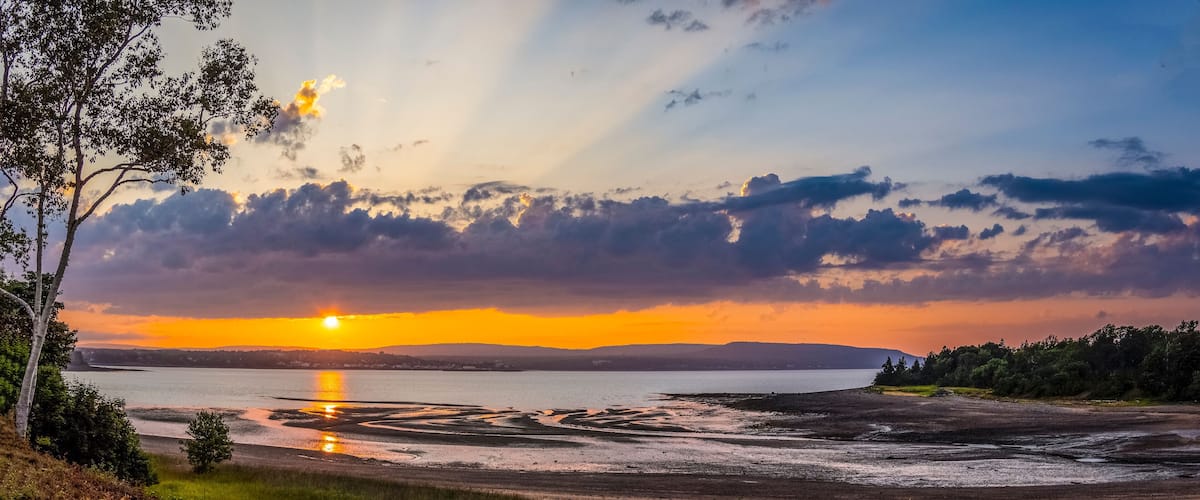 A sunset over a lake with a distant mountain range and a tree-lined shore.
