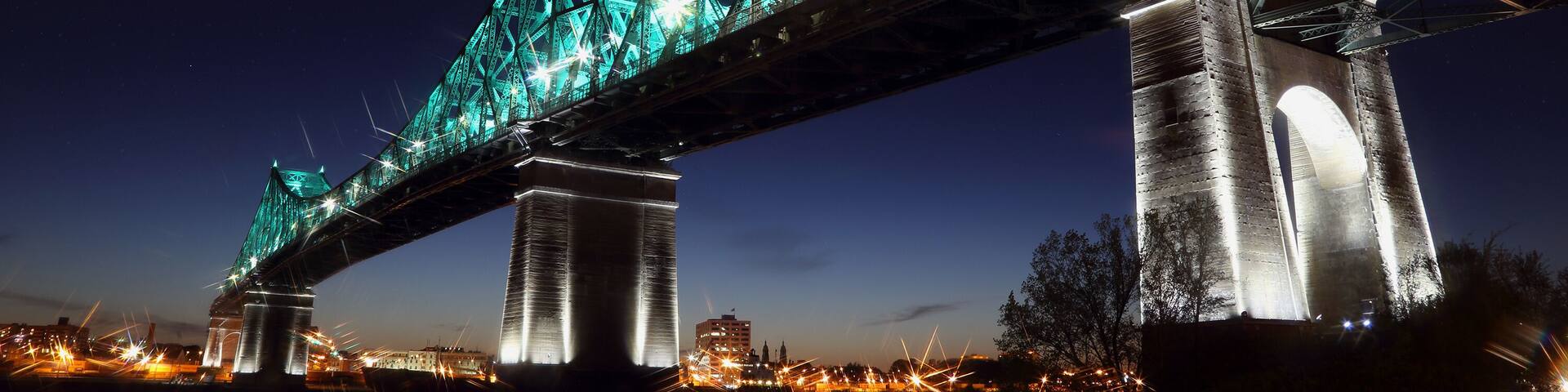 Jacques Cartier Bridge Illumination in Montreal, reflection in water. Montreal’s 375th anniversary. luminous colorful interactive Jacques Cartier Bridge. Bridge panoramic colorful silhouette by night.