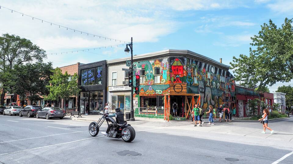 A colorful mural on a building, a street with cars, and a person on a motorcycle.