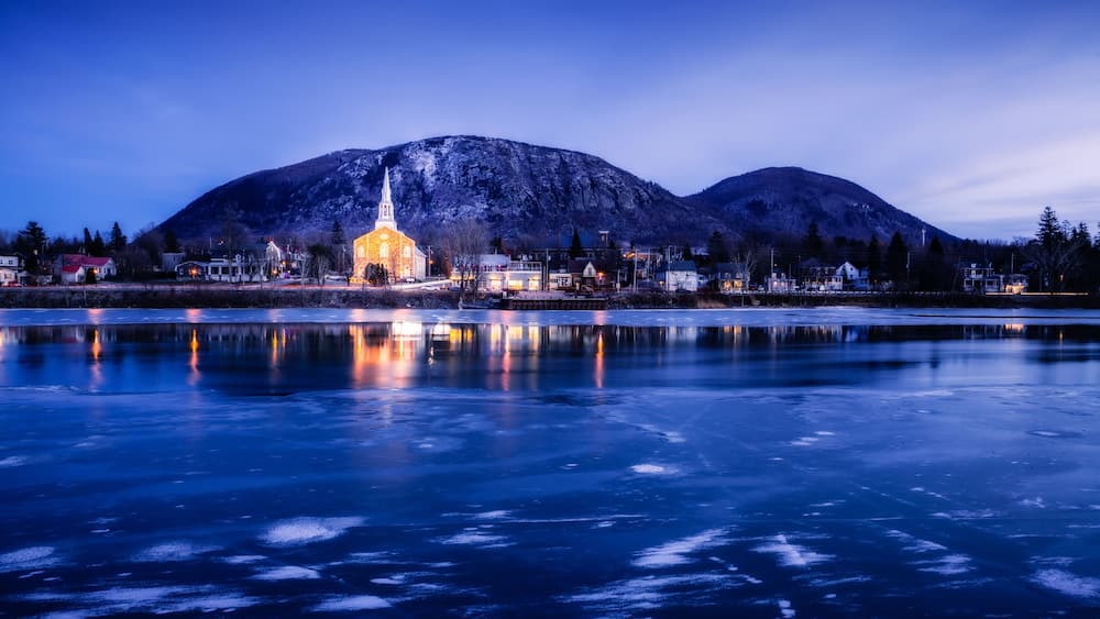A frozen lake with a church and mountains in the background.