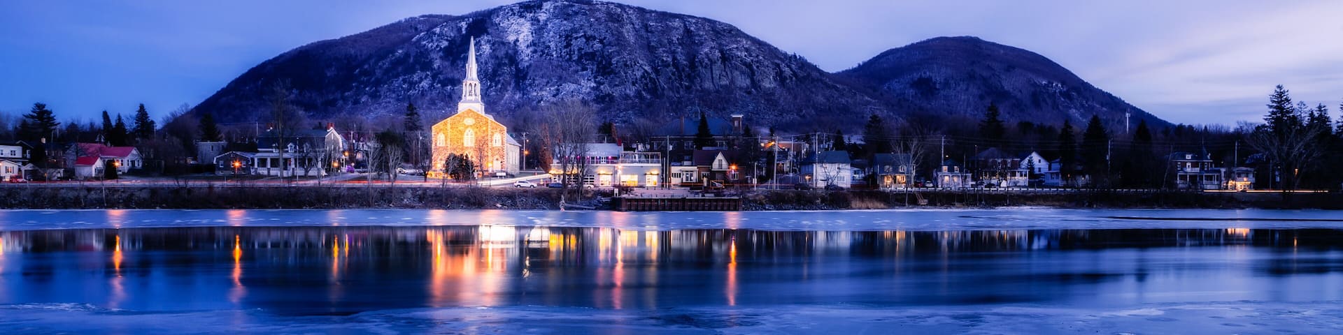 A frozen lake with a church and mountains in the background.