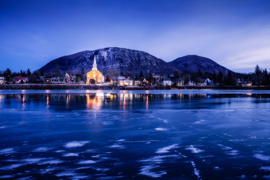 A frozen lake with a church and mountains in the background.