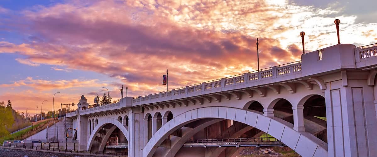 A stone bridge with arches over a river, set against a sunset sky.