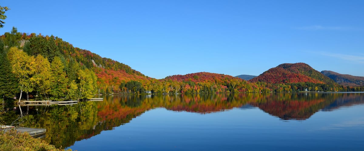 A calm lake with reflections of autumn-colored trees and distant mountains.