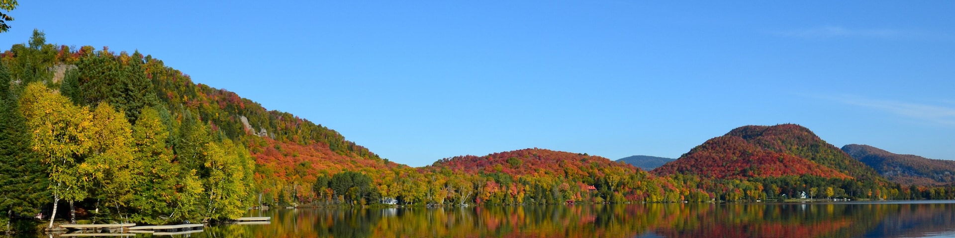A calm lake with reflections of autumn-colored trees and distant mountains.