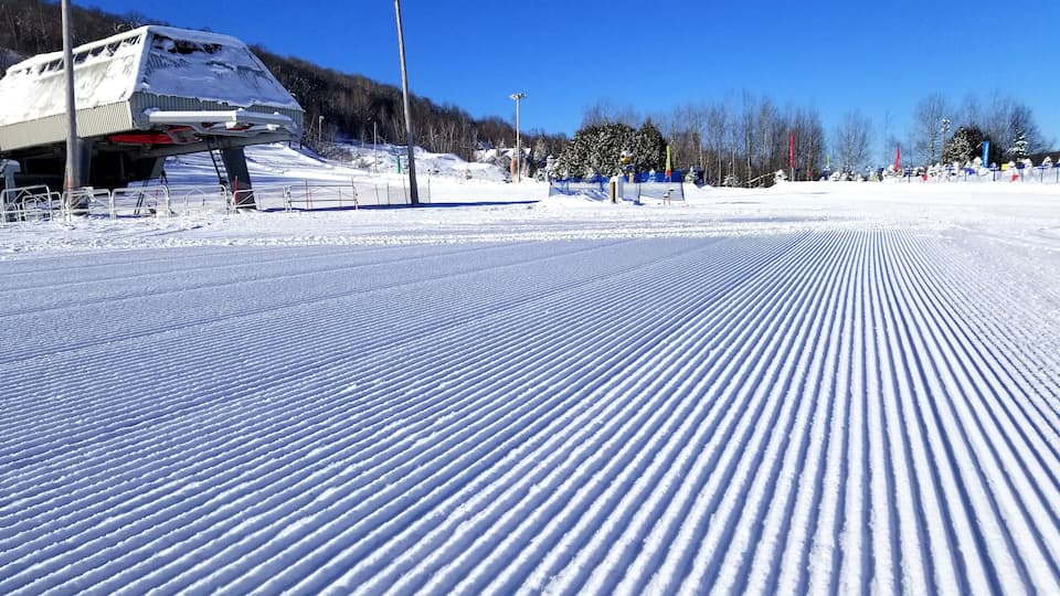 A snow-covered ski slope with a ski lift and trees in the background.