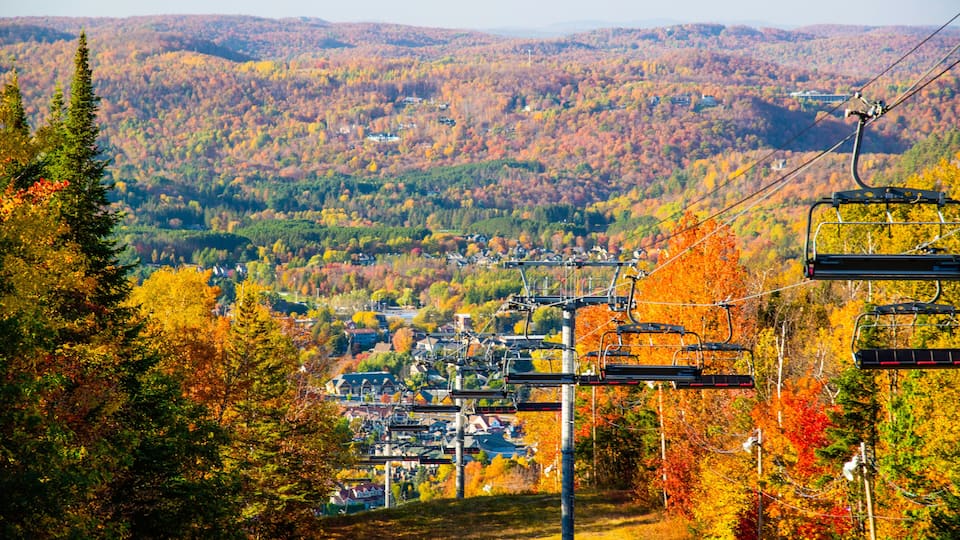 A ski lift, autumn-colored trees, and a valley town.