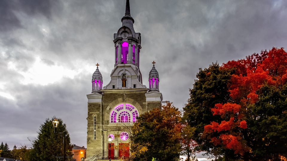 A church with a prominent steeple and arched windows, surrounded by autumn foliage.