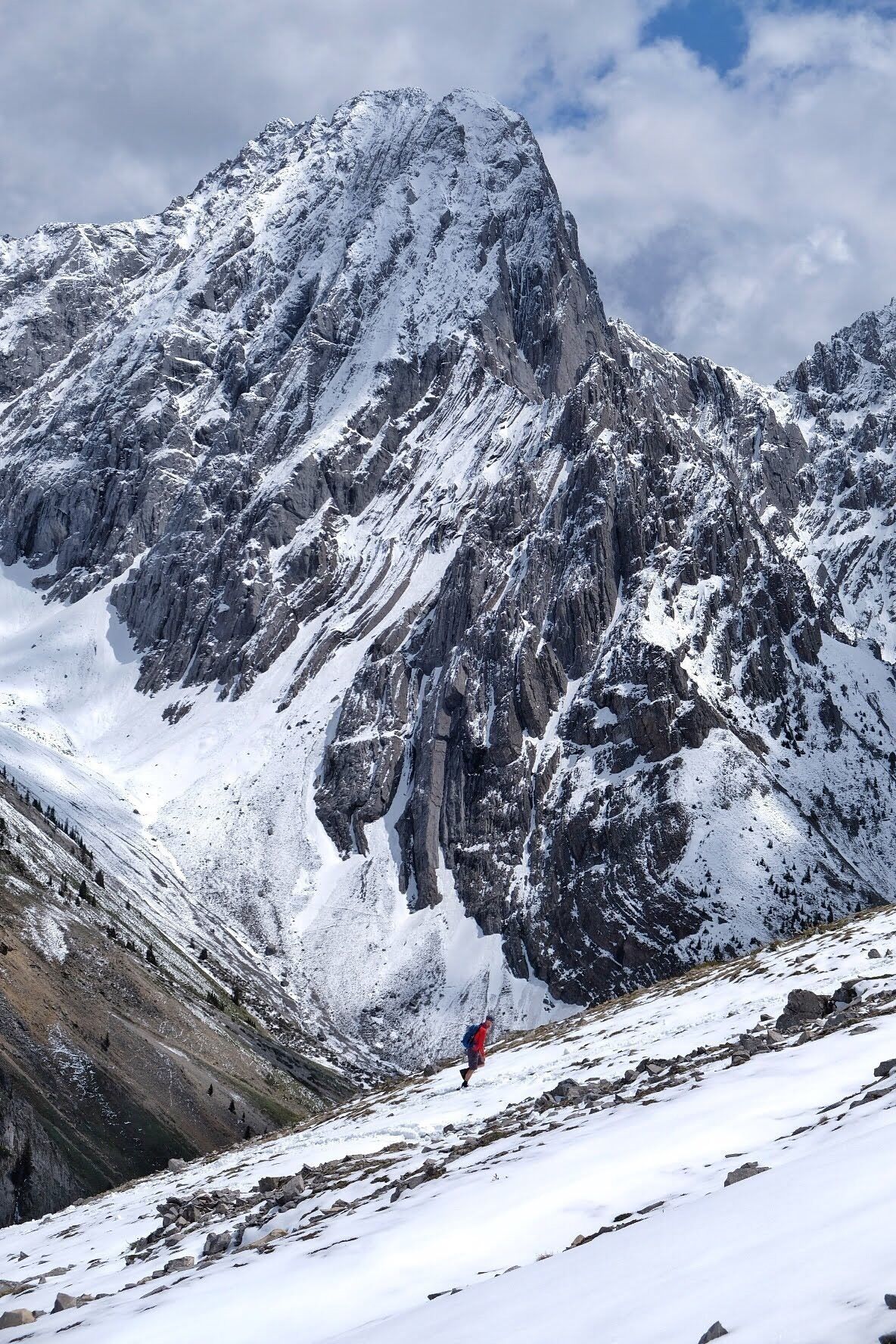 A snow-covered mountain peak with a climber in red at the base.