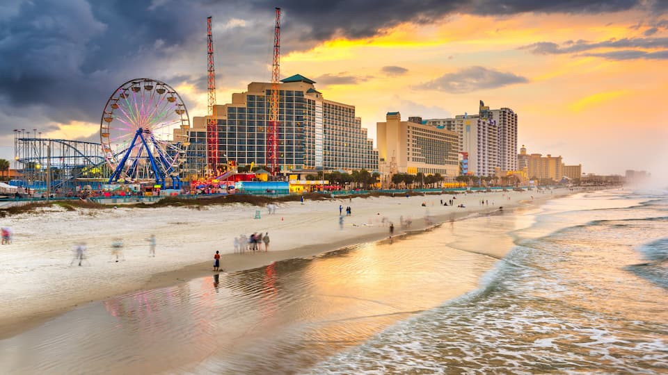 A beach with a Ferris wheel, a tall red crane, and a hotel complex.