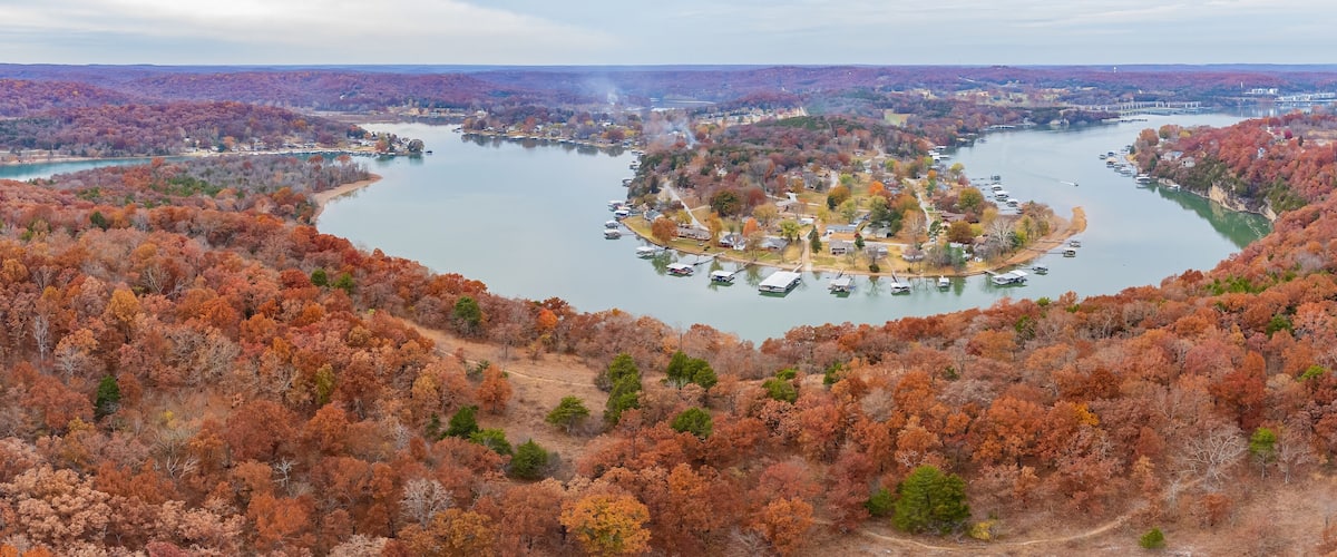A river surrounded by autumn-colored trees, a small island with docks, and a distant bridge.