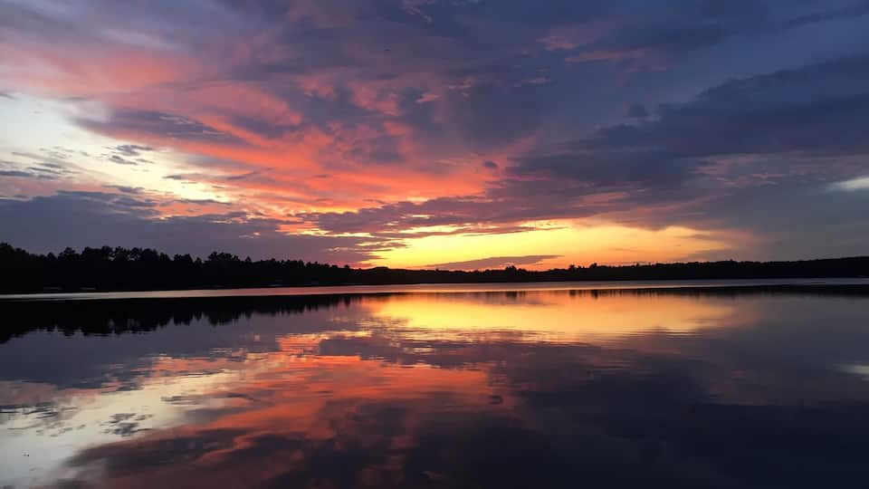 A sunset over a calm lake with a forest silhouette in the background.