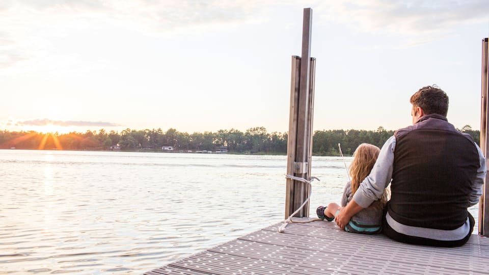 Caucasian father and daughter sitting on pier at sunset