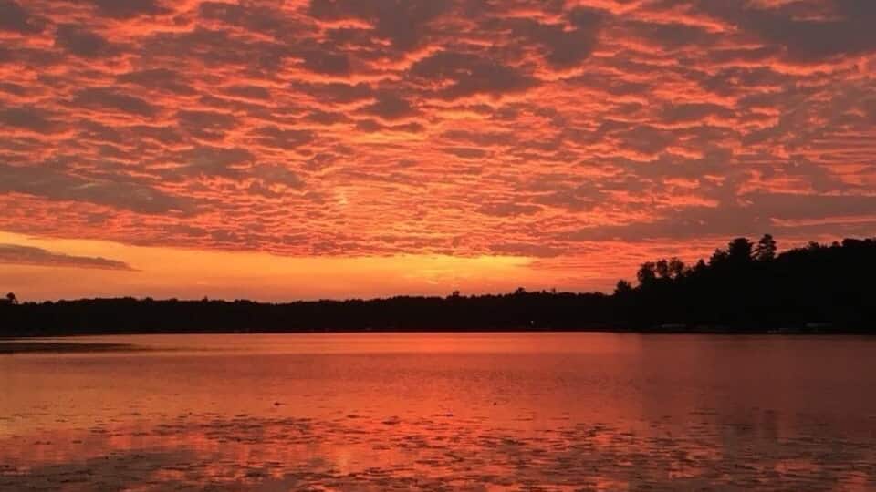 A sunset over a lake with a red sky and calm water.