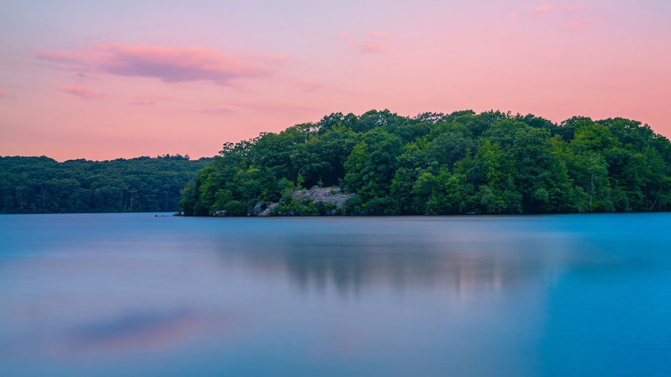 Sunset and dramatic cloudscape over the lake with green forest, water lilies, and reflections at Lincoln State Park in Providence, Rhode Island