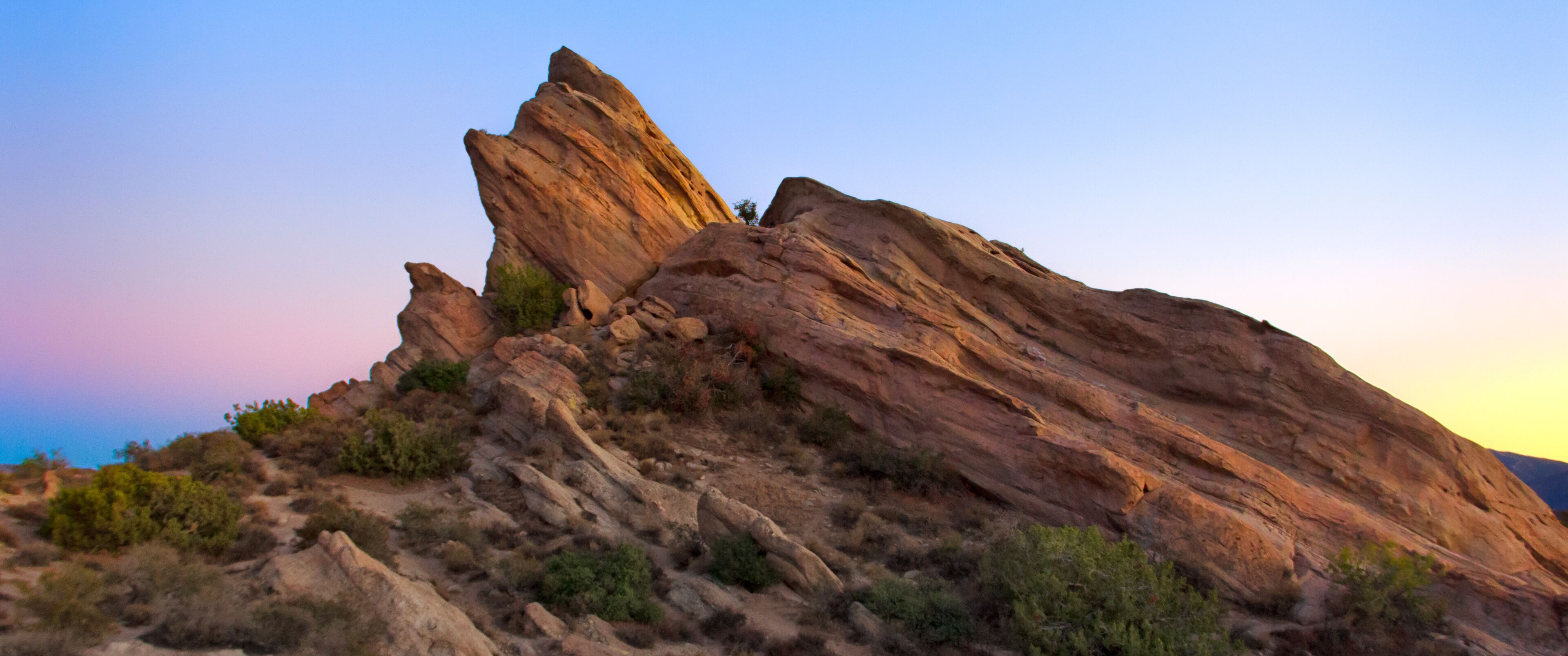 A rugged rock formation with a prominent peak, surrounded by sparse vegetation.