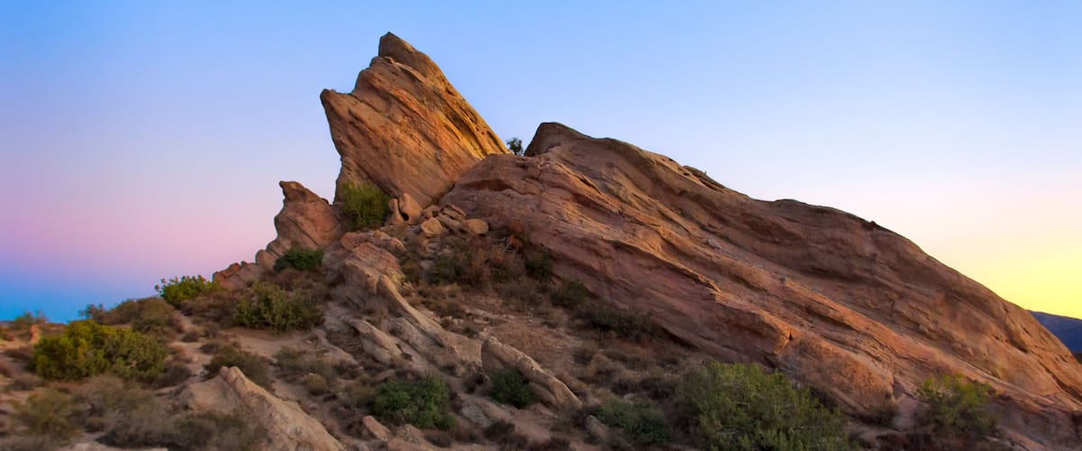 A rugged rock formation with a prominent peak, surrounded by sparse vegetation.