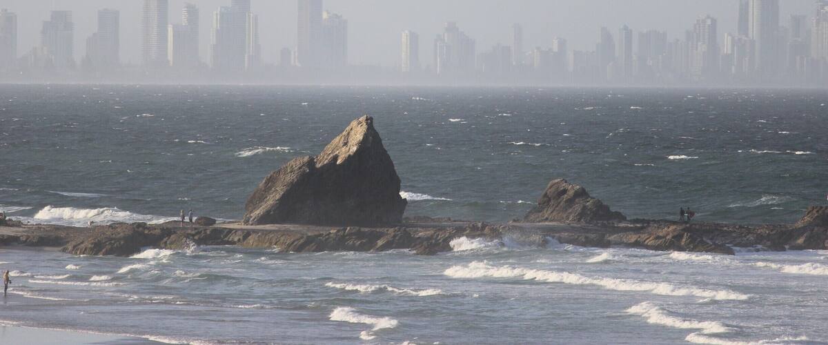 A coastal cityscape with a rocky shoreline and waves crashing against the rocks.