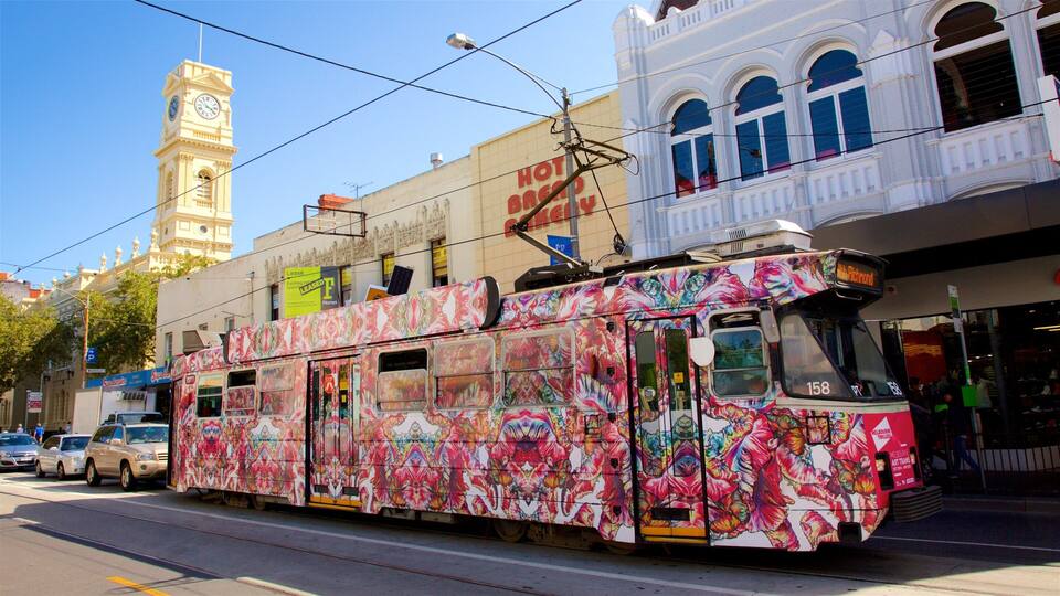 Um elétrico colorido com padrões florais, uma torre do relógio e um edifício com o letreiro 'HOT BAGELS'.