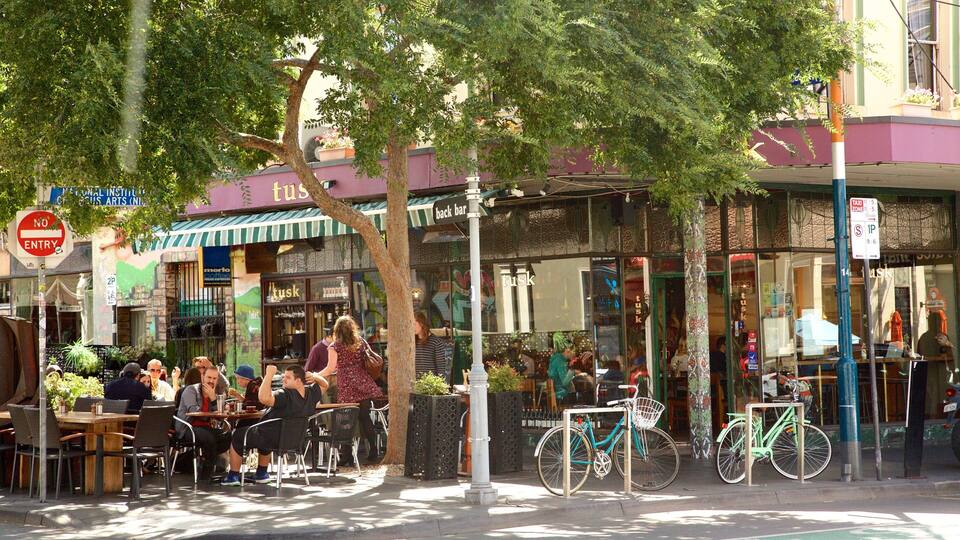 Um café ao ar livre movimentado, com mesas e cadeiras, bicicletas estacionadas perto e um aviso de 'Proibido o Acesso' visível.