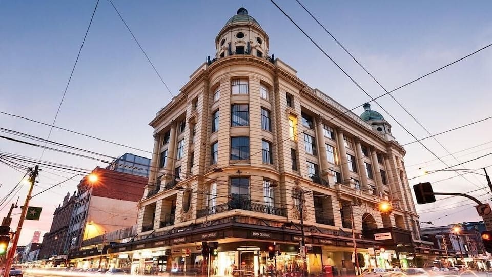 Um edifício histórico com cúpula e vários andares, situado numa praça movimentada com luminárias e semáforos.