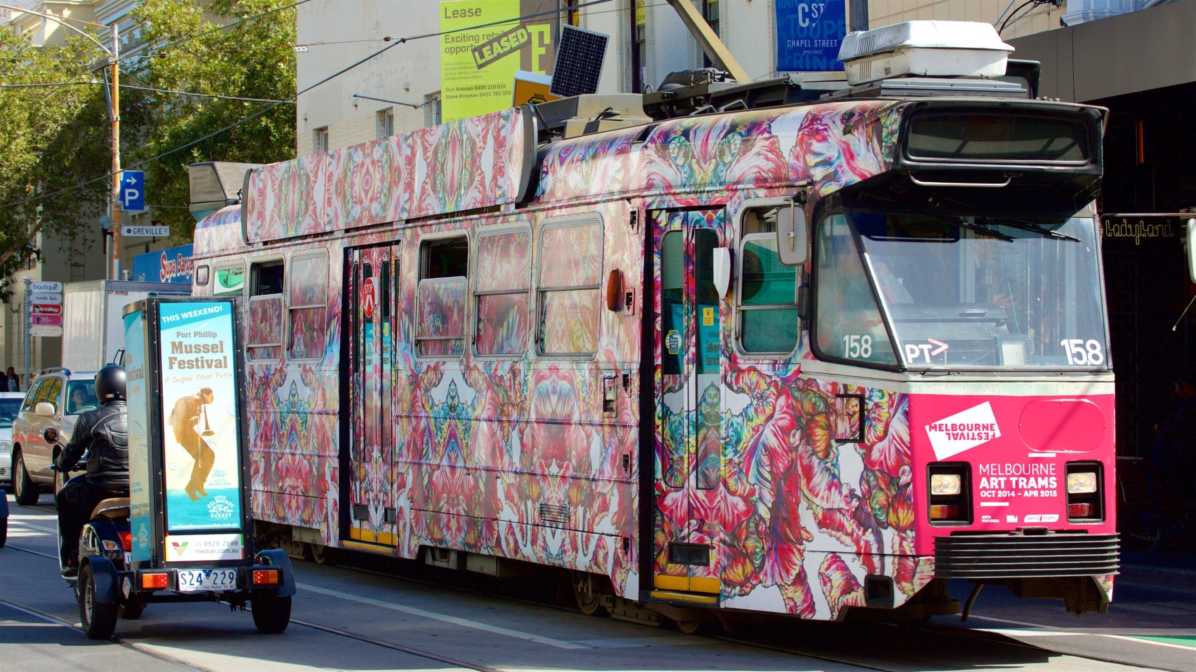 Un tranvía colorido con un diseño de mural vibrante, circulando por una calle de la ciudad.