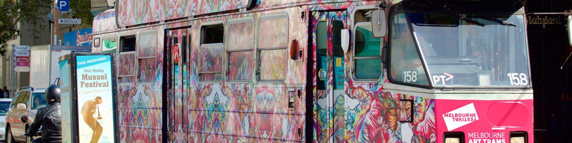 Un tranvía colorido con un diseño de mural vibrante, circulando por una calle de la ciudad.