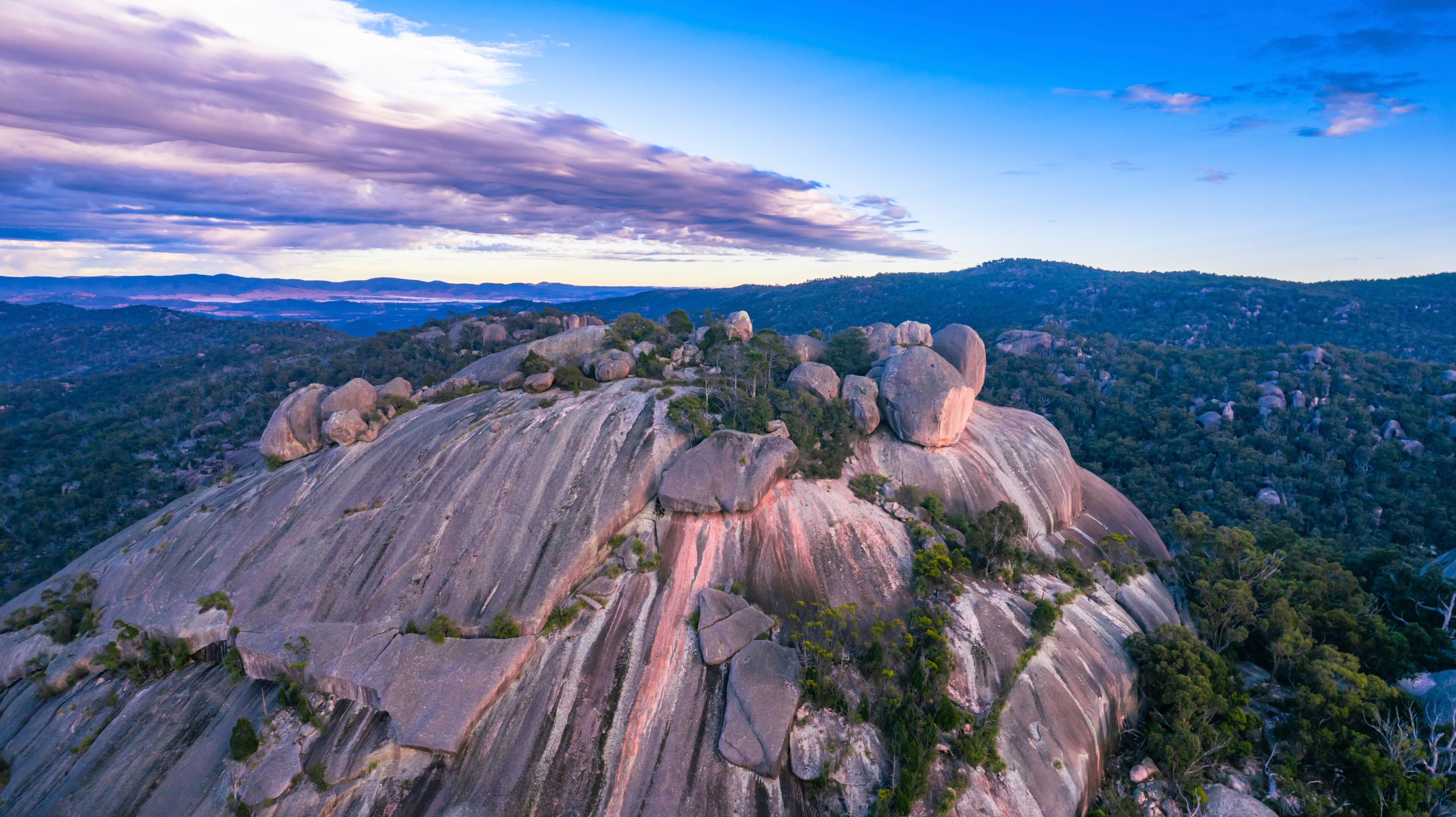 A large rock formation with a forested mountain range in the background.