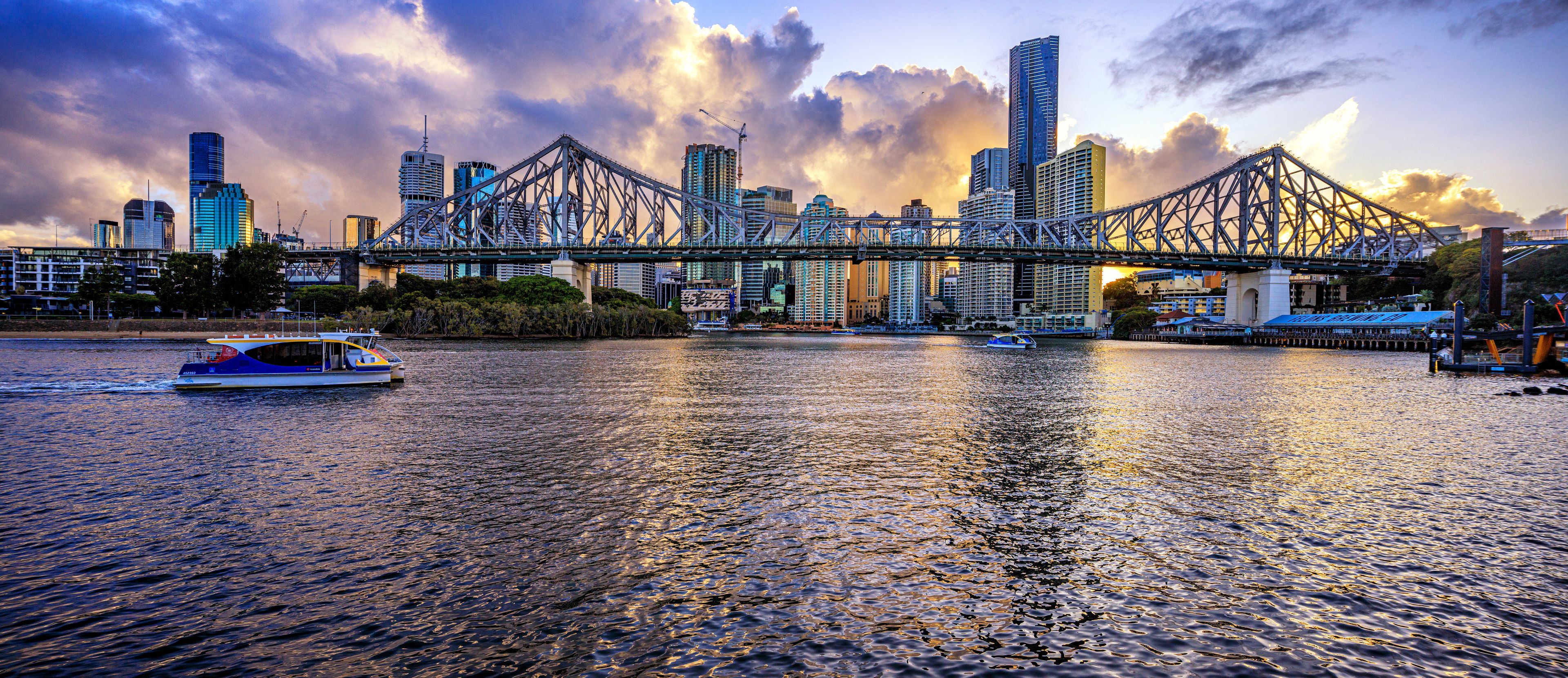 A river with a bridge, boats, and a city skyline with tall buildings.