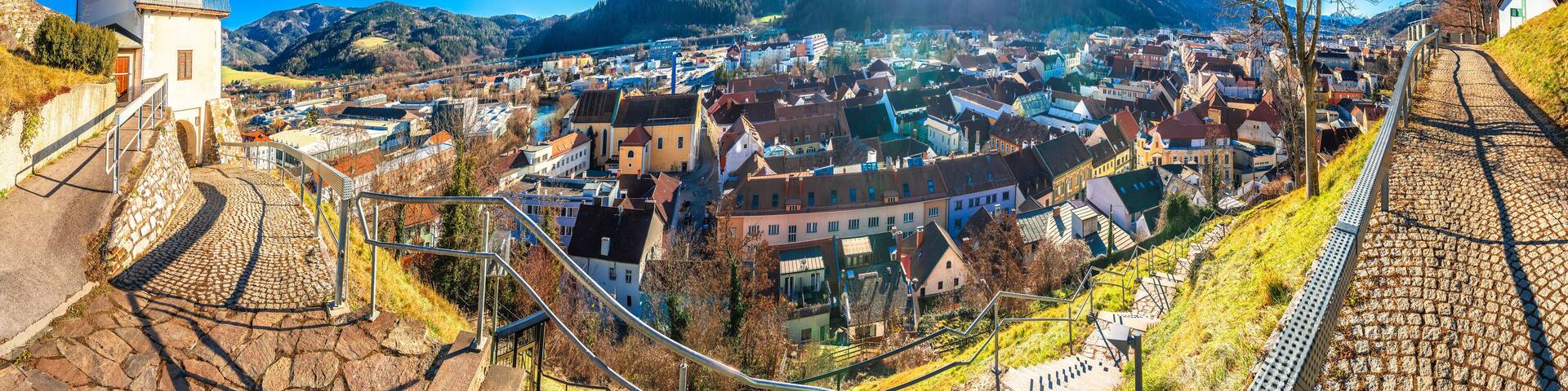 A town with a clock tower, cobblestone streets, and mountains in the background.