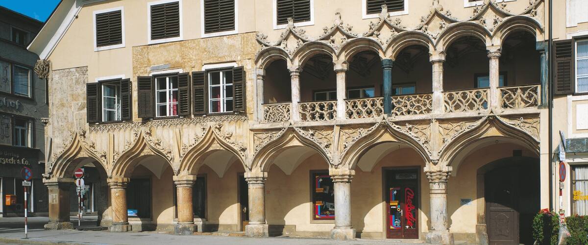 A historic building with ornate Gothic arches and a balcony with intricate metalwork.