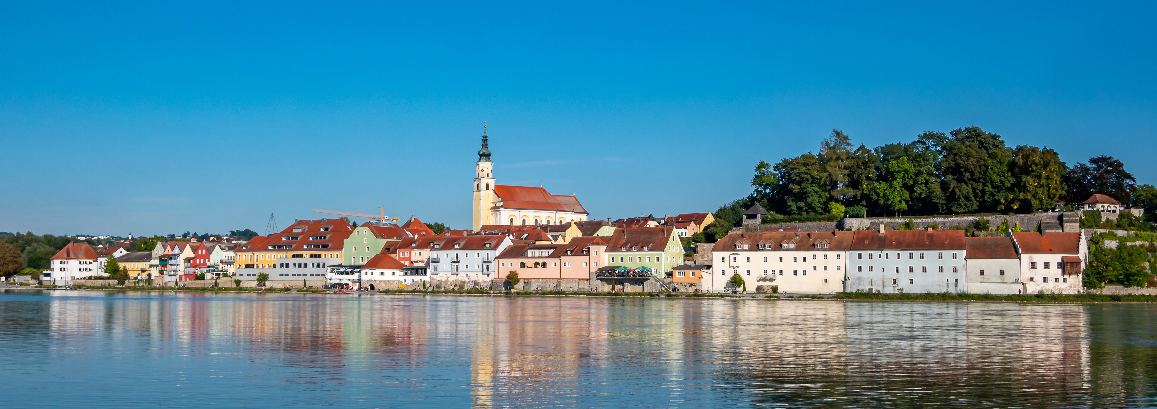 A riverside town with colorful buildings, a prominent church tower, and a castle on a hill.