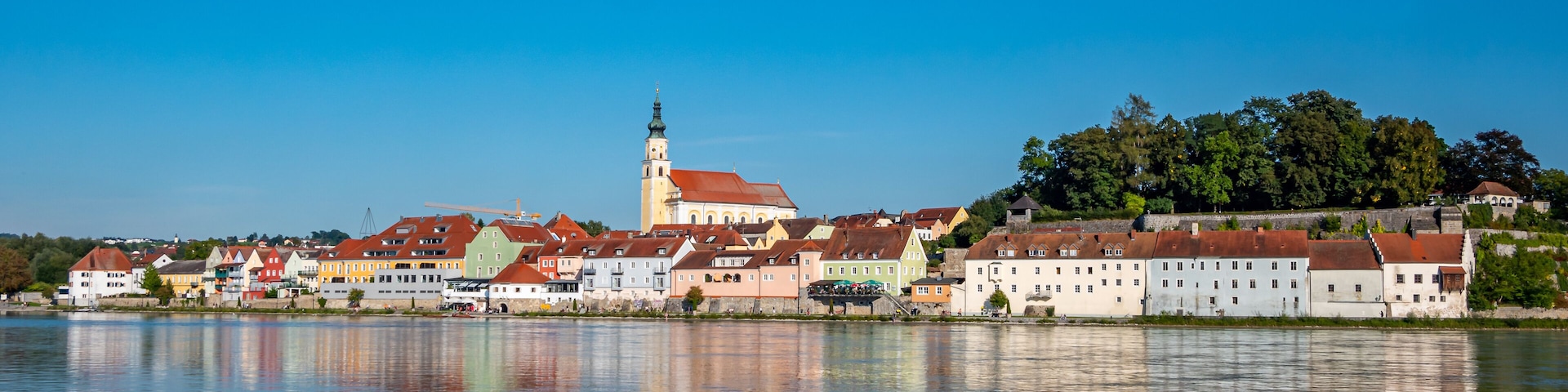 A riverside town with colorful buildings, a prominent church tower, and a castle on a hill.