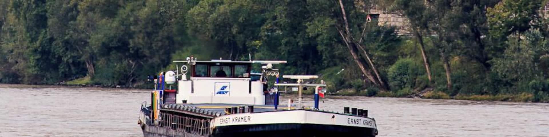 A boat named 'Ernst Kummer' on a river, a church with a tall tower, and a hillside with vineyards.