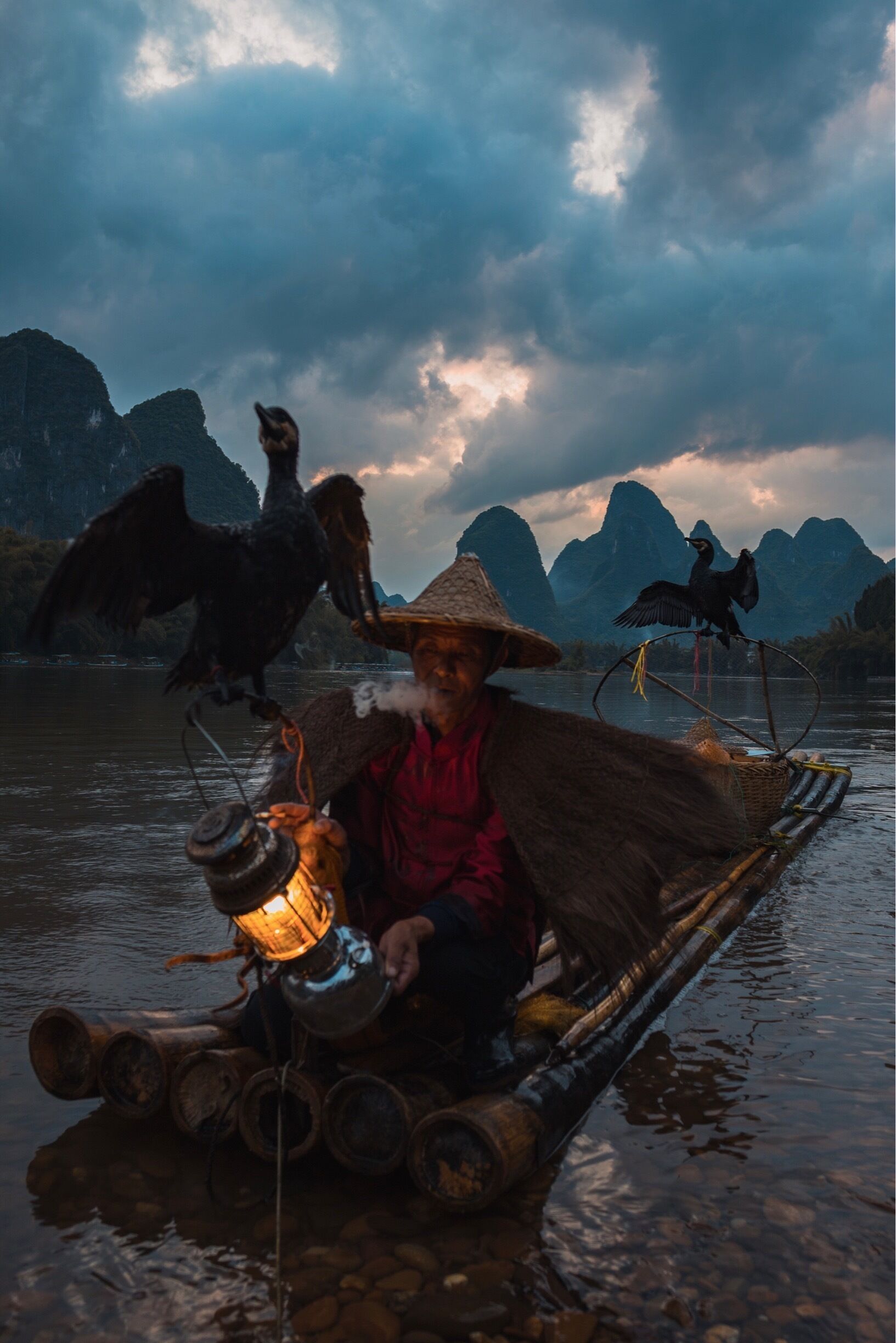 A person in a traditional boat with a lantern, surrounded by mountains and birds.