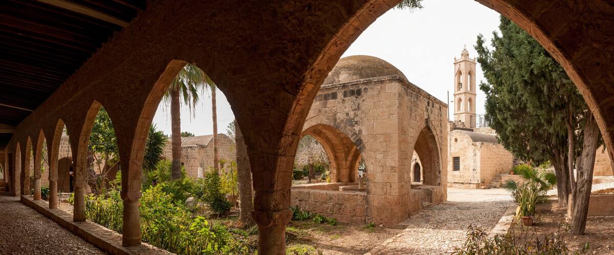 An ancient stone corridor with arches, a church with a dome, and a bell tower.