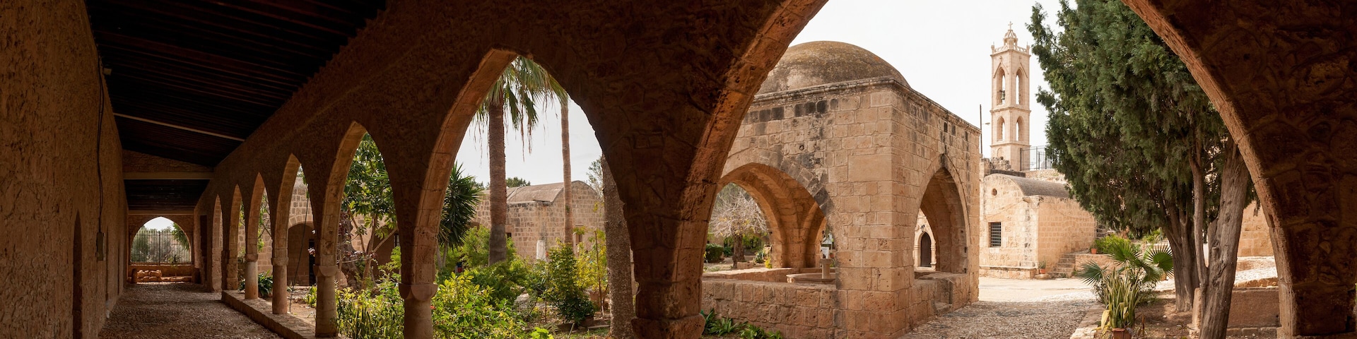 An ancient stone corridor with arches, a church with a dome, and a bell tower.